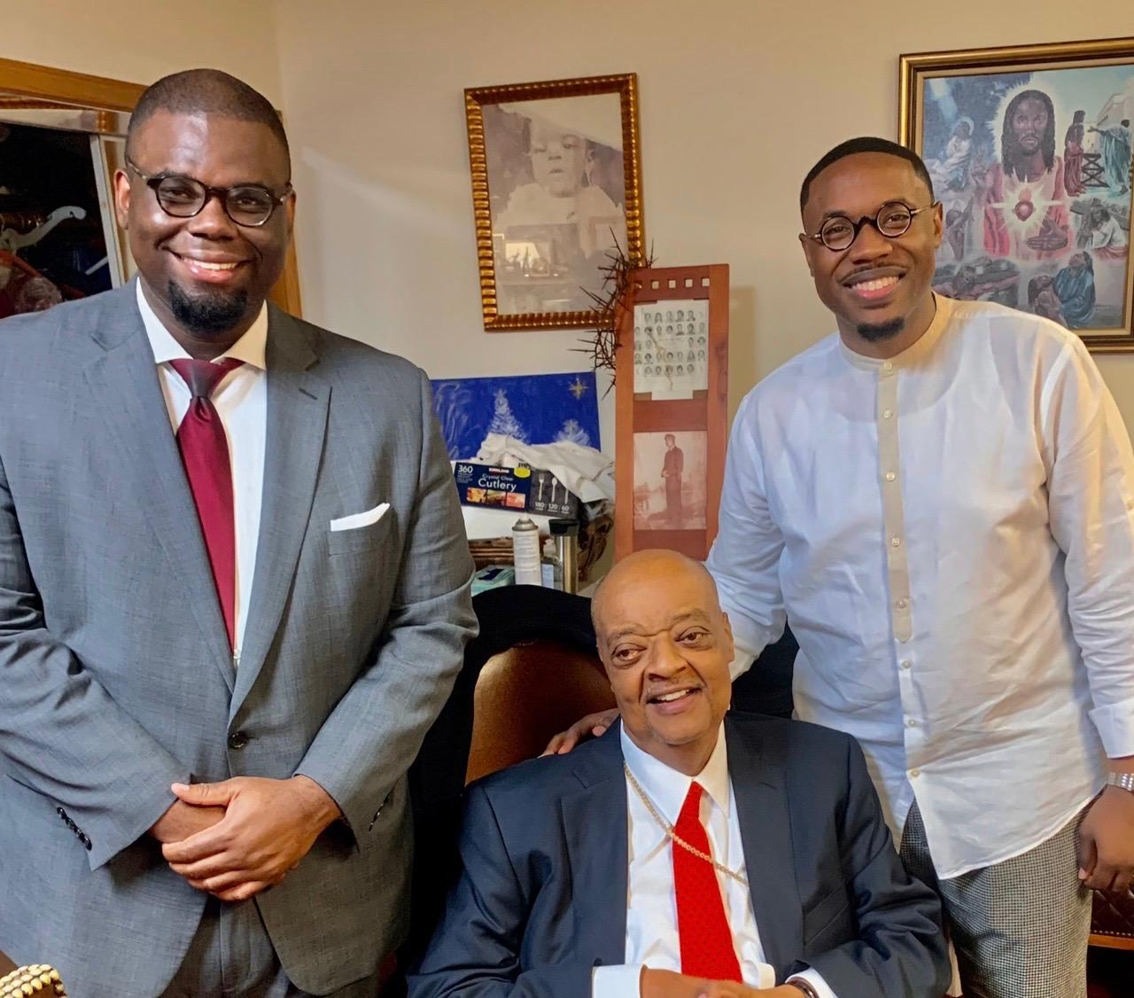 Three ministers together in a study, one seated in a chair