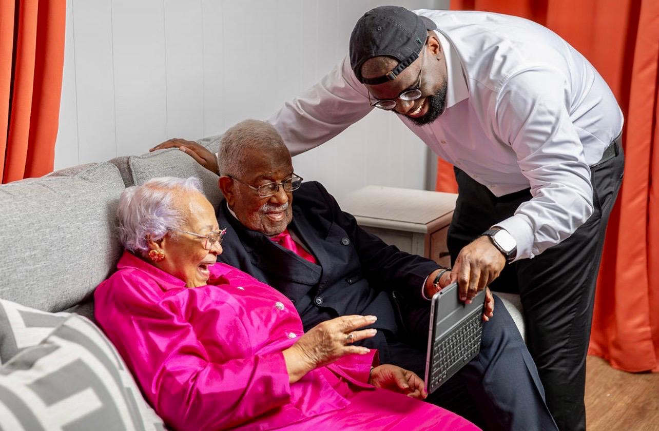 Jeremy Q. Henry showing a tablet to an elder couple seated on a sofa