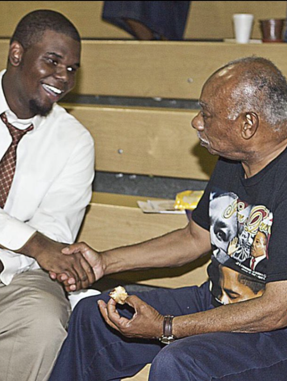 A younger Jeremy Q. Henry shaking hands with an elder at a community gathering