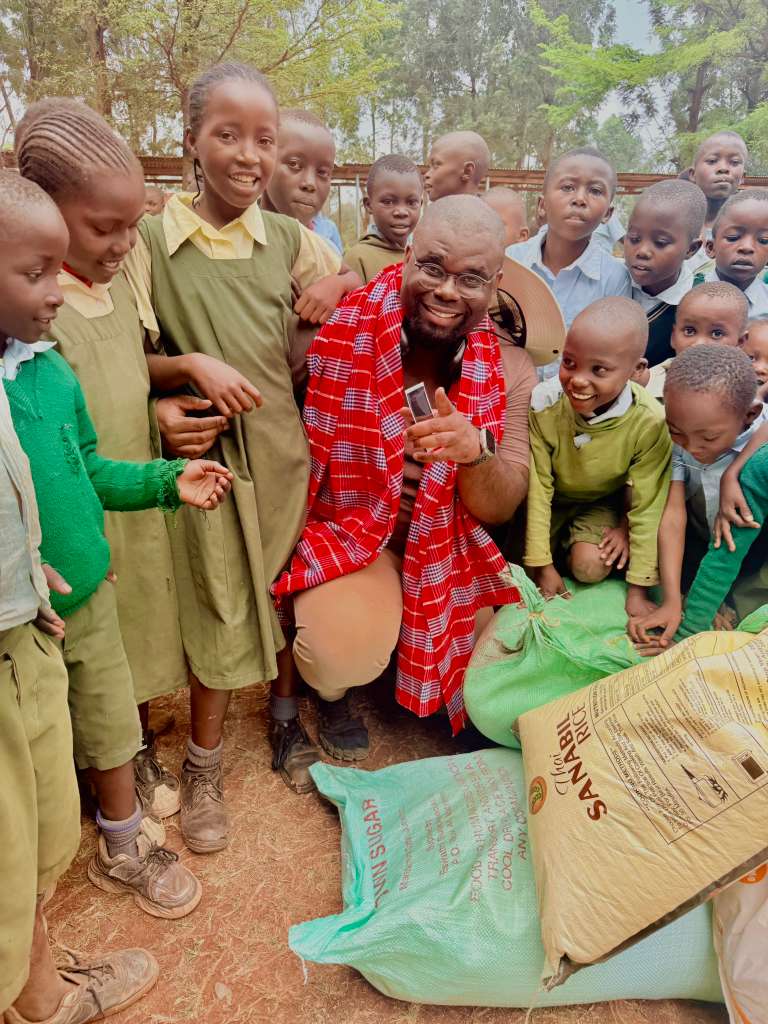 Jeremy Q. Henry kneeling with schoolchildren in Kenya beside sacks of rice and sugar